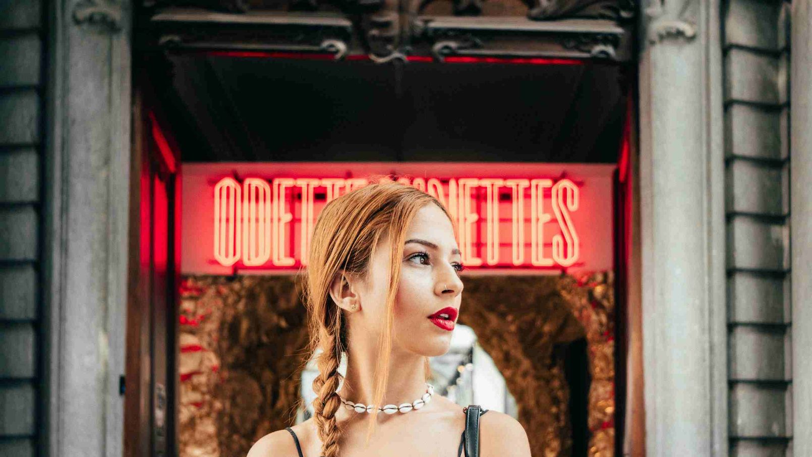 霓虹灯牌前的女子侧脸，红光落在编起的长发与颈间项链上